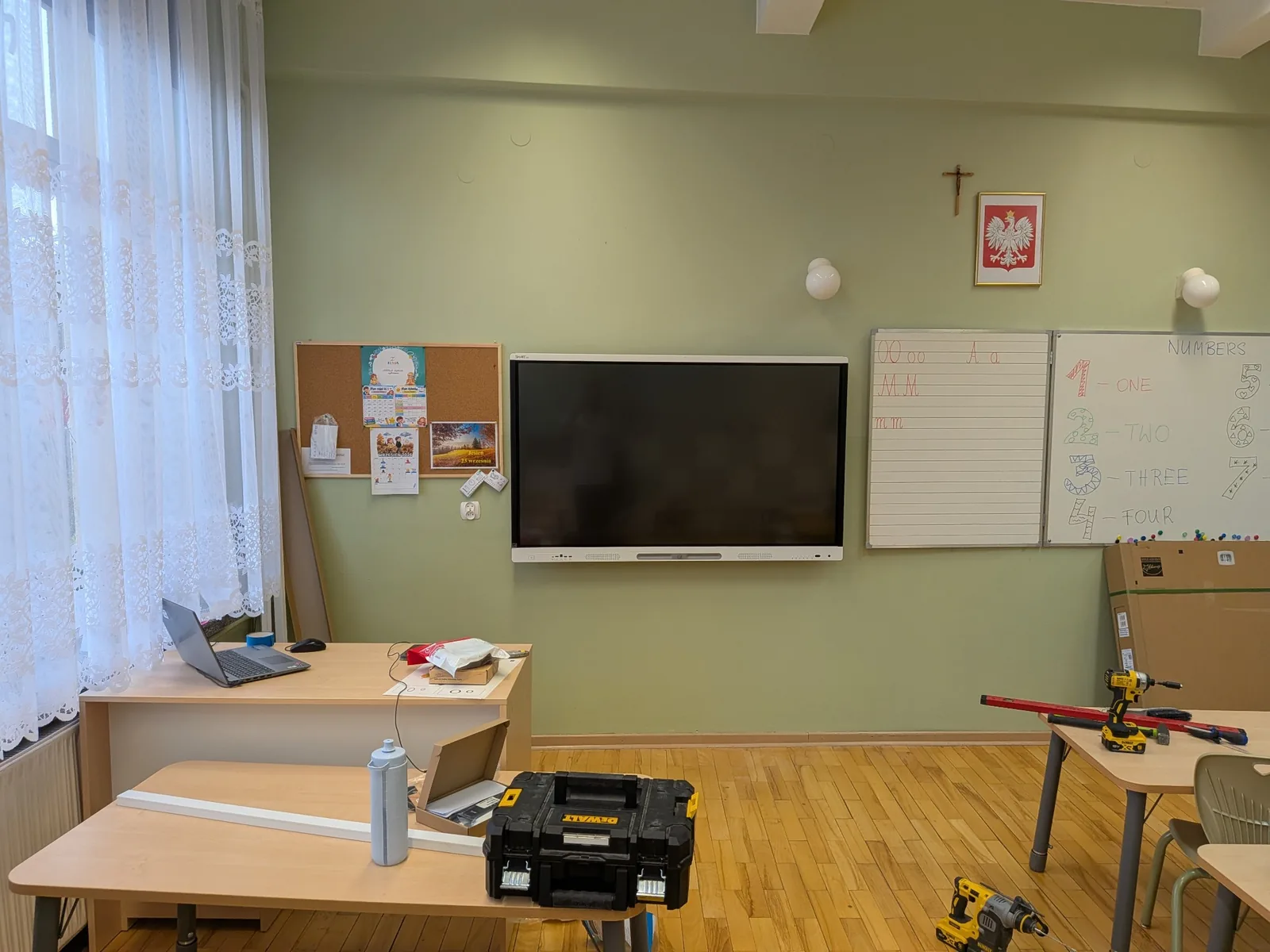 Zawieszony monitor SMART z wyłączonym ekranem, obok tradycyjnej tablicy i biurka nauczyciela.